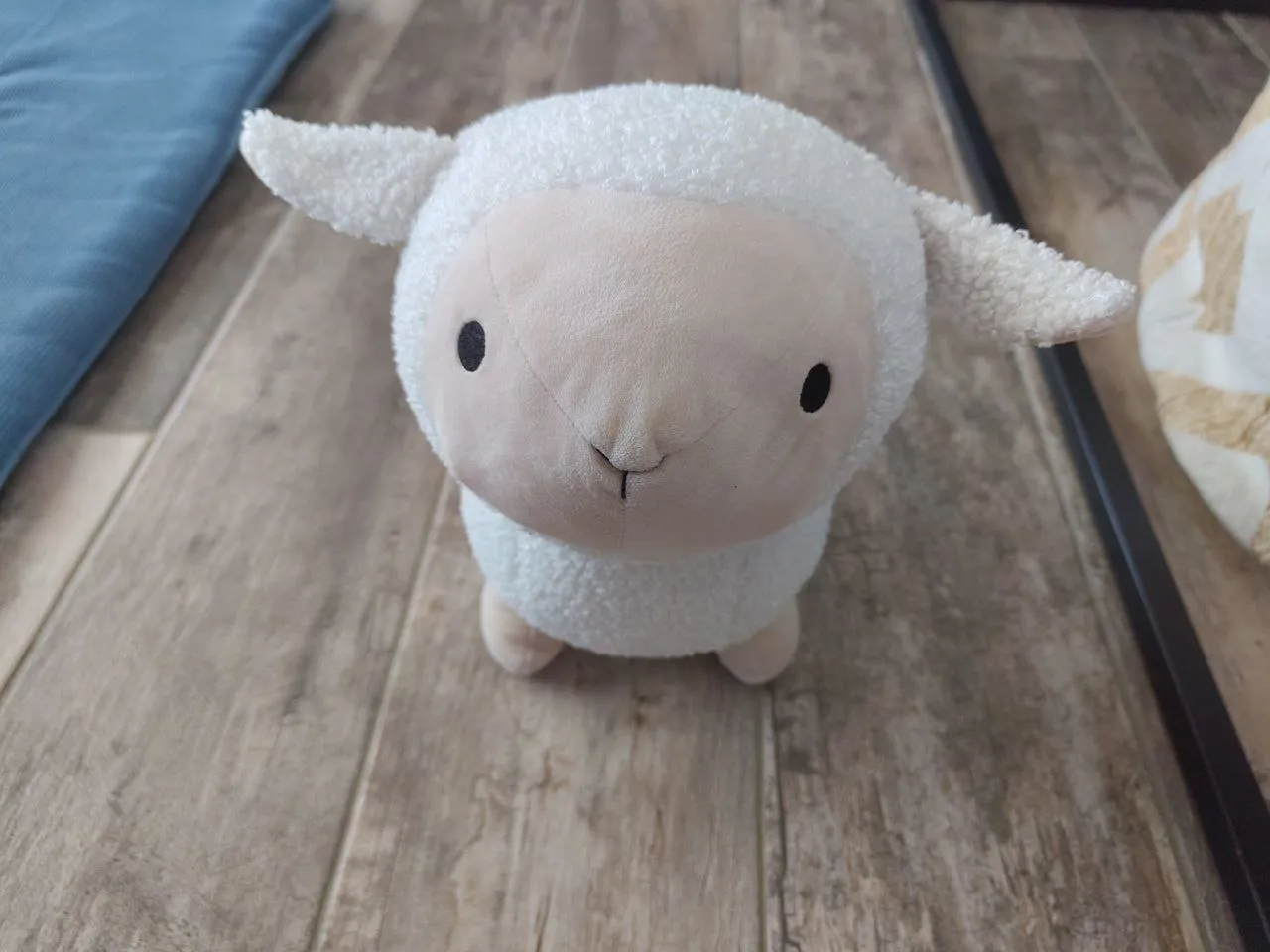 A plush sheep toy facing forward on a wooden surface
